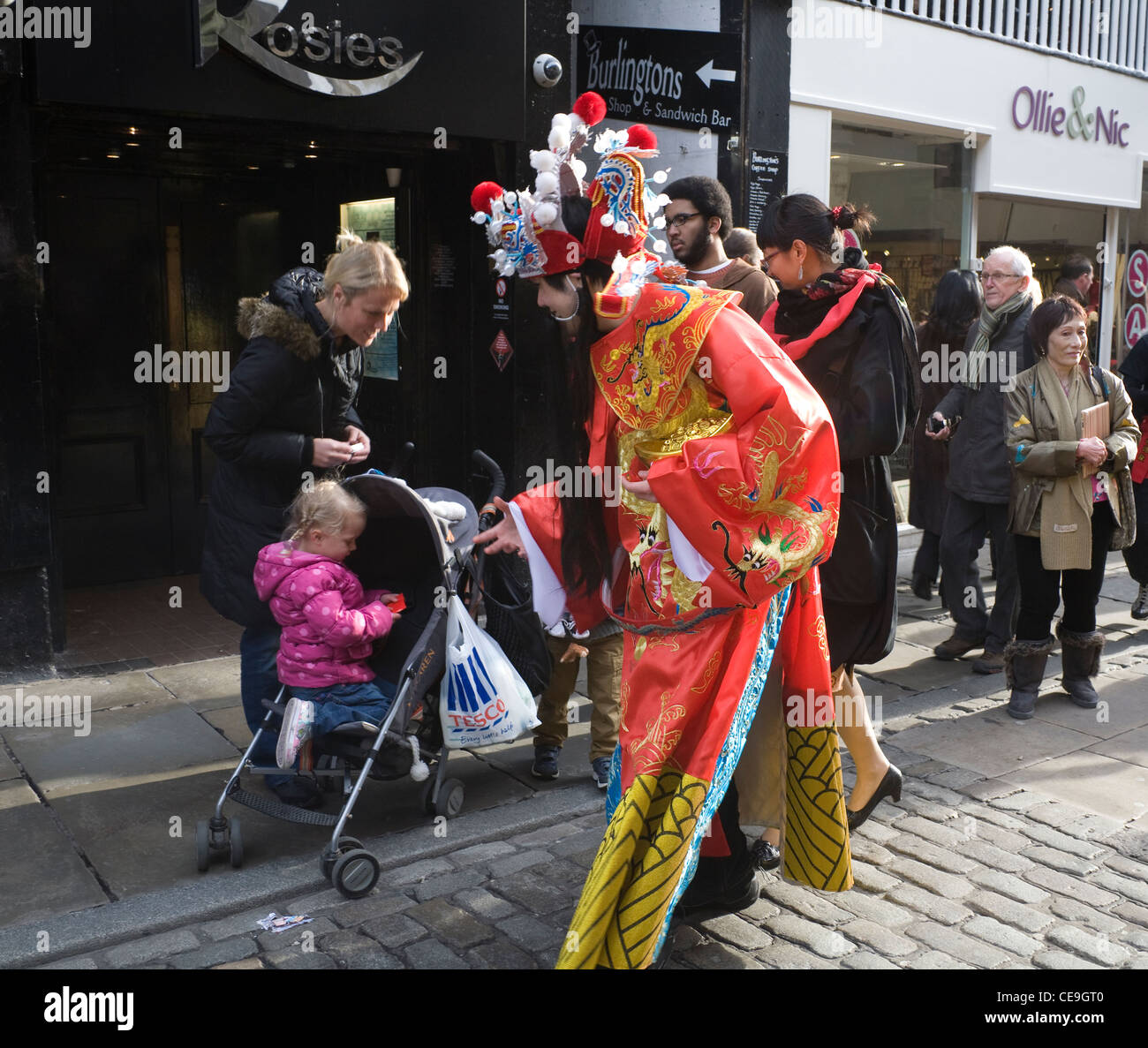 Chester Cheshire uomo vestito in abiti di seta al nuovo anno cinese parade Anno del Dragone consegna busta rossa al bambino passeggino Foto Stock
