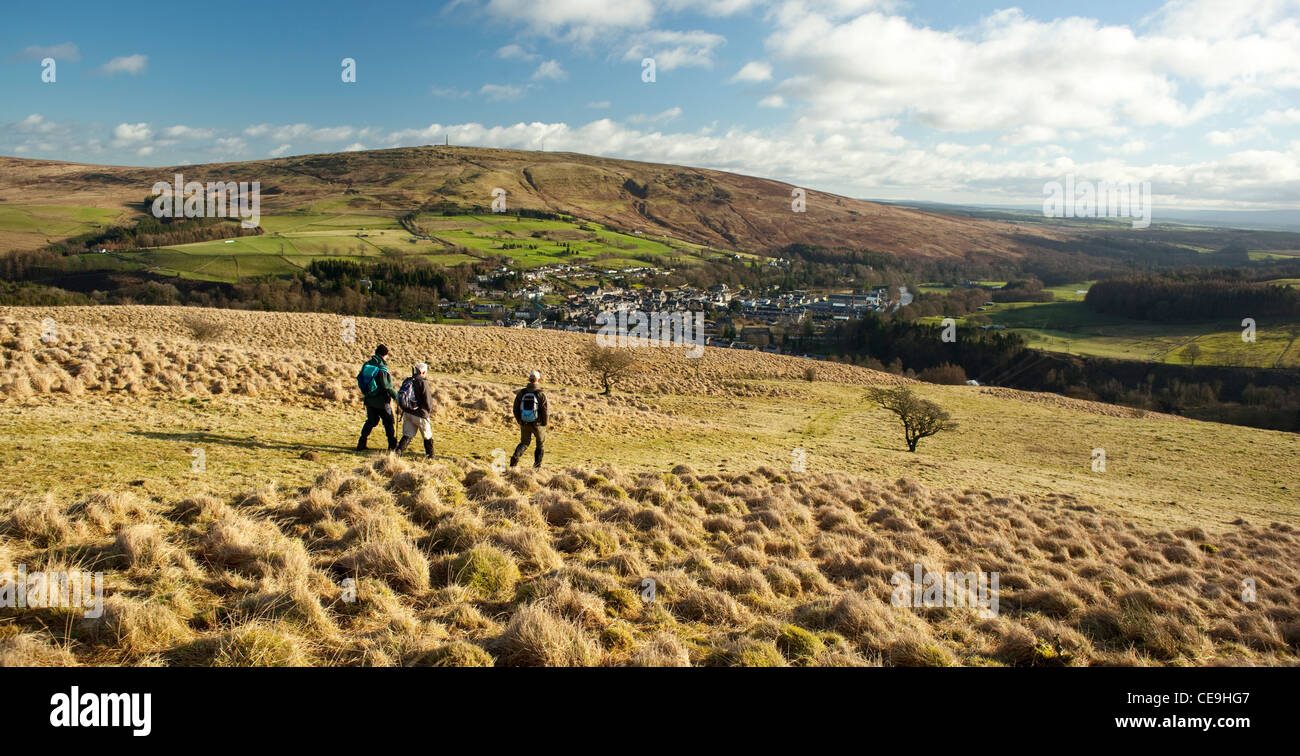Escursionisti invernali camminate fuori Meiklehom Hill lookng giù sulla città di Langholm sulla frontiera scozzese con Whita collina dietro scozzese Foto Stock