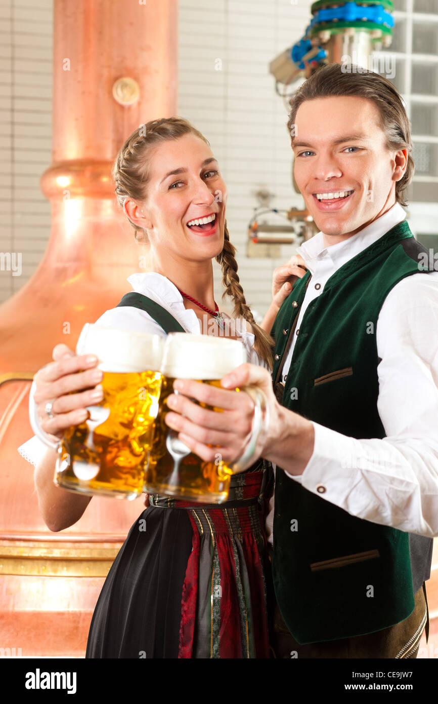 Uomo e donna con bicchieri da birra in Baviera tracht in birreria di fronte ad un bollitore brew Foto Stock
