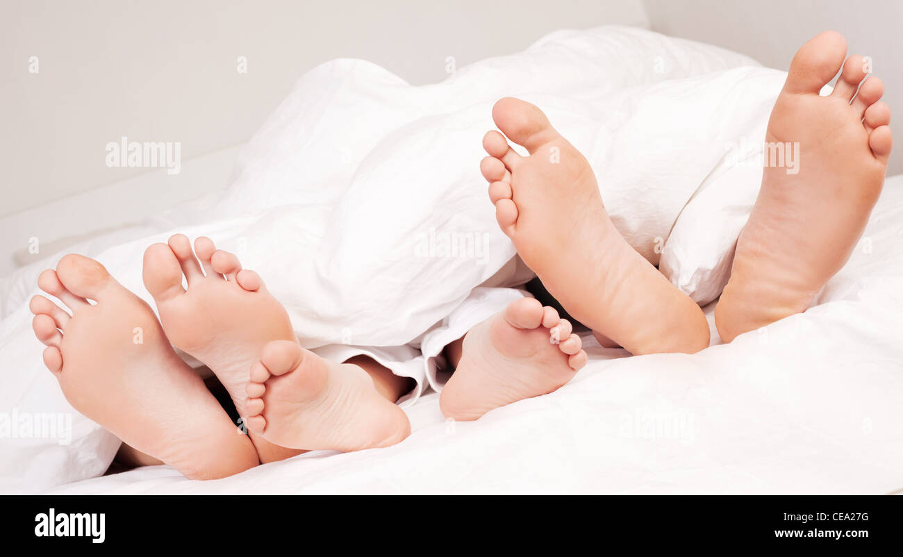 La famiglia felice; i piedi di una madre ,padre e il loro figlio sotto la balnket nel letto di casa Foto Stock