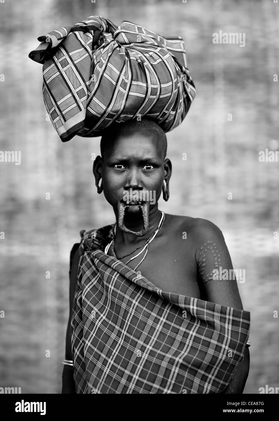 Scarified Mursi donna con il prolungamento del labbro inferiore e lobi auricolari trasporta un carico sul suo capo con la paura di guardare Valle dell'Omo Etiopia Foto Stock