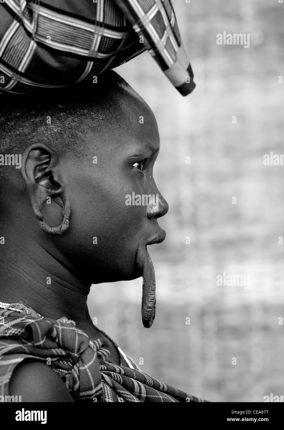 Mursi donna con il prolungamento del labbro inferiore e lobi auricolari trasporta un carico sul suo capo Valle dell'Omo Etiopia Foto Stock