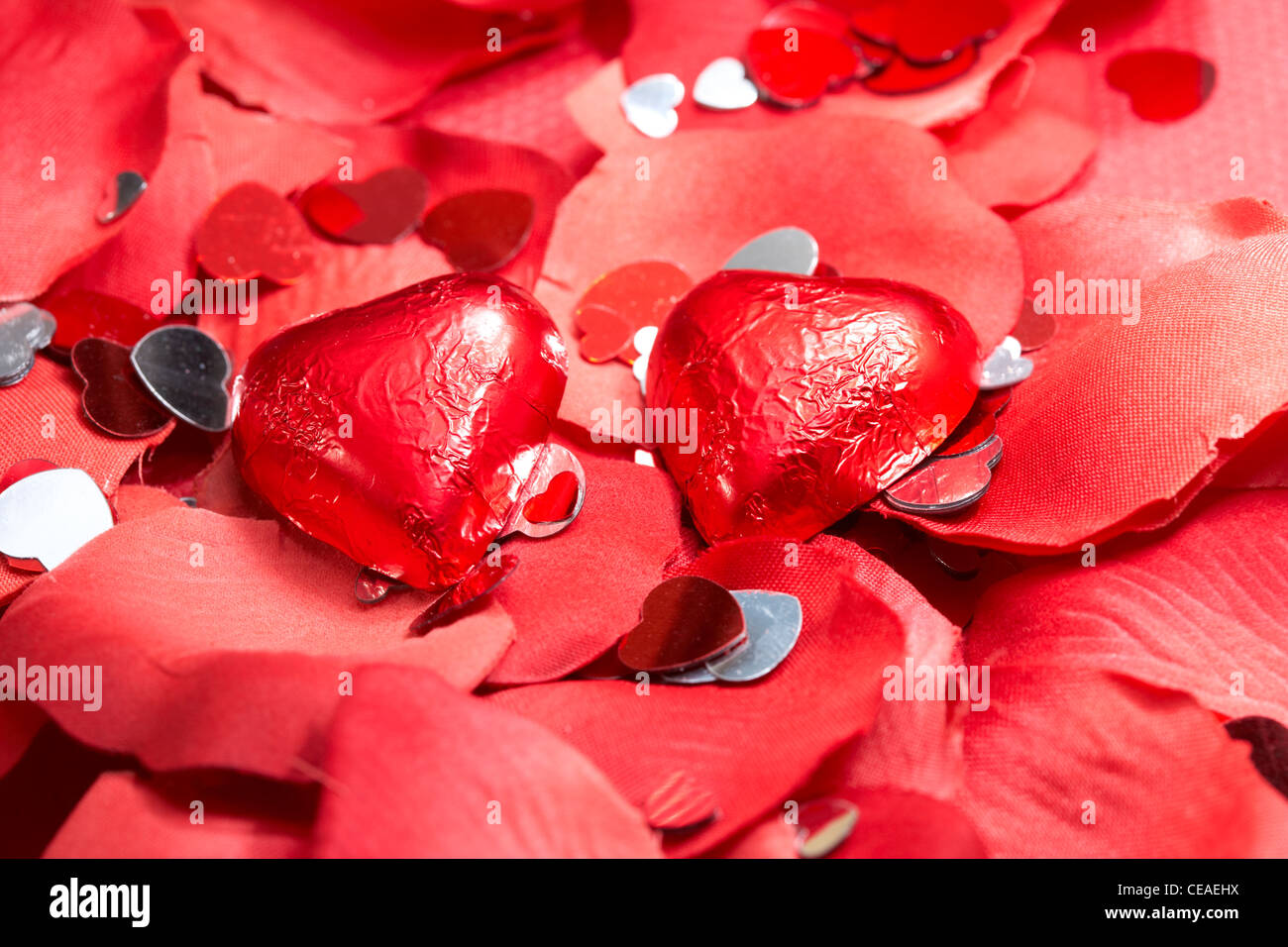 Cuori di cioccolato su falsi petali di colore rosso con decorazioni di cuore Foto Stock