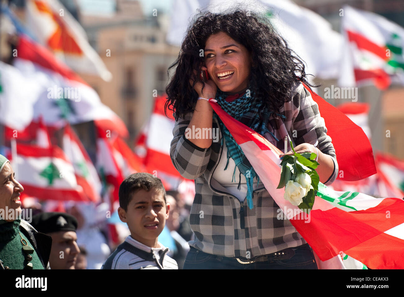 Giovane donna sorrisi ampiamente e colloqui sul telefono cellulare, circondato da bandiere, durante la politica dei rally a Beirut, in Libano. Primavera araba Foto Stock