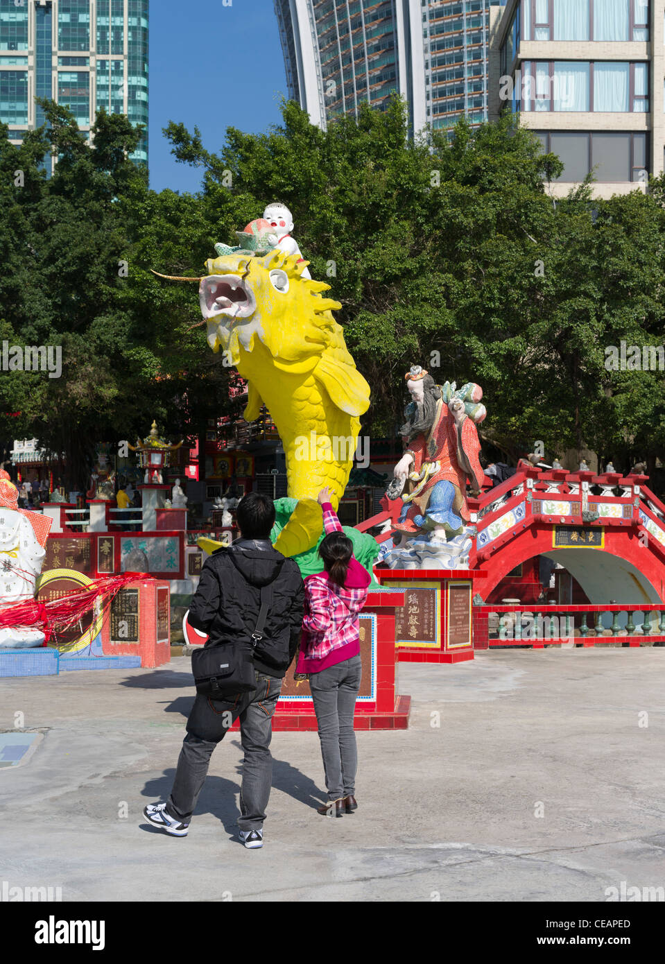 dh REPULSE BAY HONG KONG ragazza cinese e ragazzo gettando soldi in Fish of Prosperity statua bocca buona fortuna tao Foto Stock
