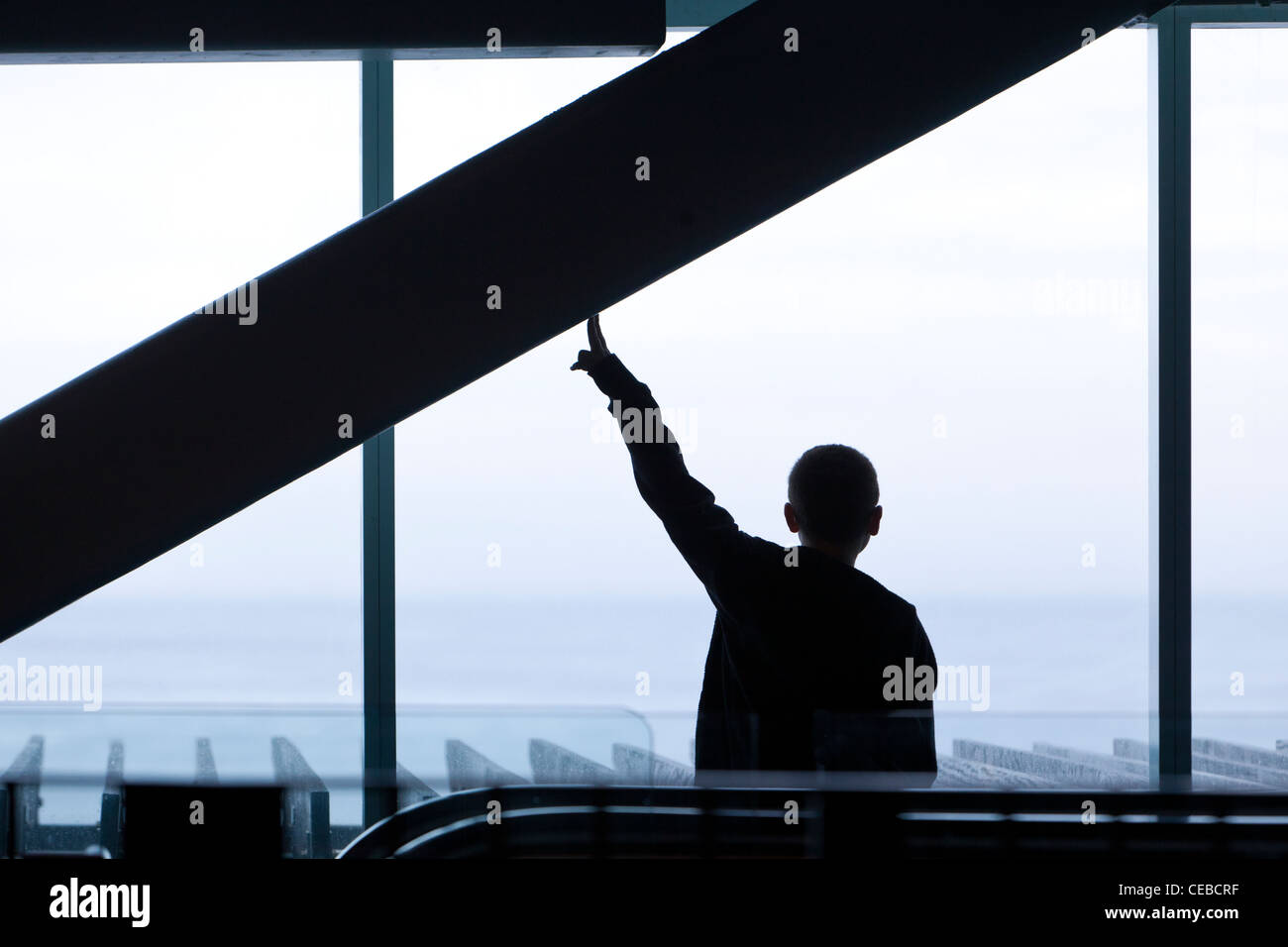 Una silhouette di un giovane uomo in piedi in un centro commerciale Mall contro un cielo luminoso. Foto Stock