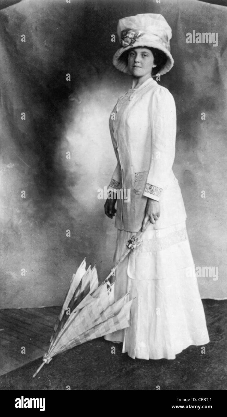 Donna che indossa piede-lungh.. abito e cappello e ombrello di contenimento con la punta sul pavimento.! Circa 1910 Foto Stock