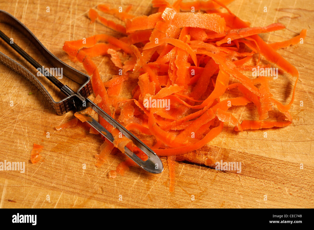 Un pelapatate e bucce di carota giaceva su un legno tagliere. Foto Stock