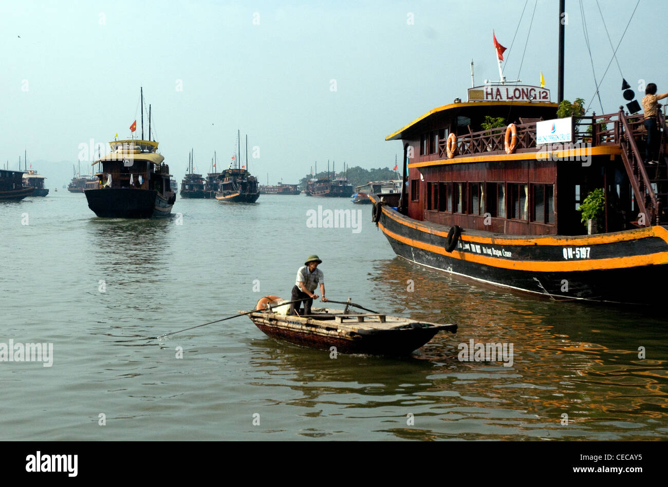 In Vietnam la baia di Ha Long una barca a remi contrasta con giunche convertito al di ancoraggio vicino al porto principale Foto Stock
