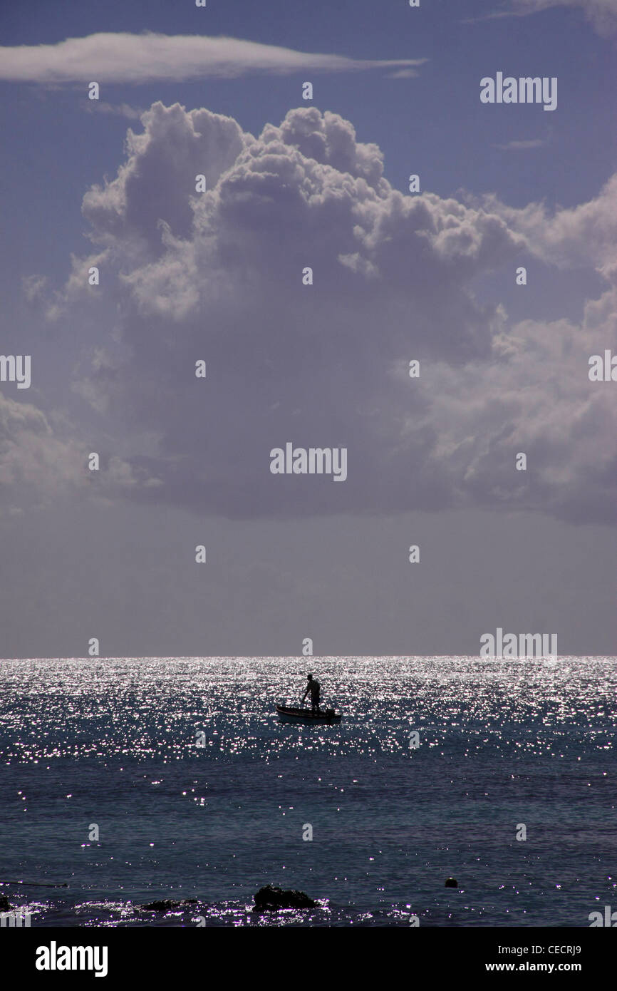 Un uomo in silhouette su una piccola barca sul mare dei Caraibi a Barbados, West Indies. Foto Stock