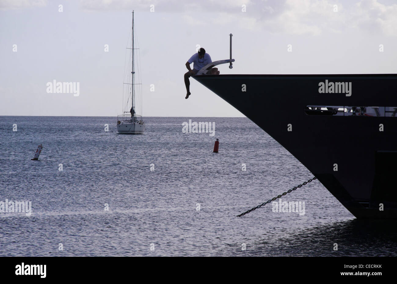 Un uomo in silhouette pende la sua gamba come lui pulisce uno yacht di lusso a Port St Charles, Barbados, West Indies. Foto Stock