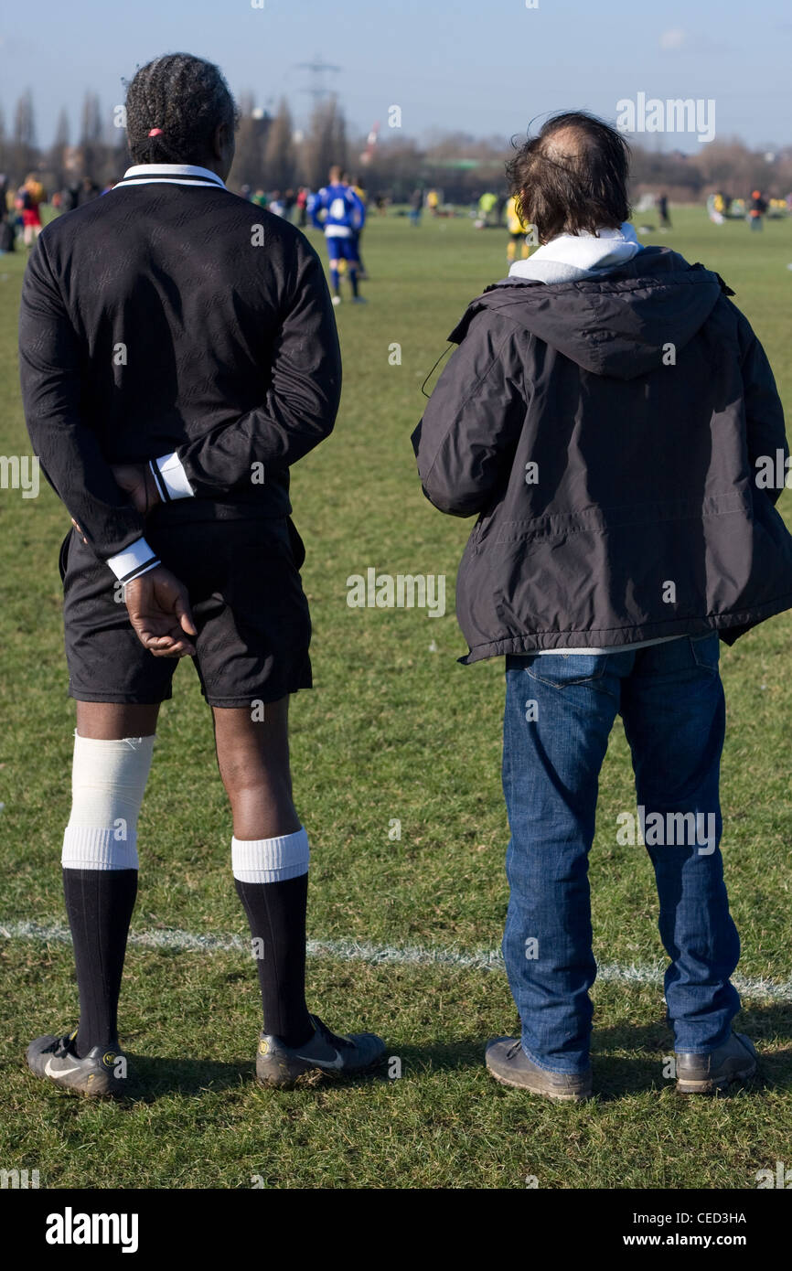 Un arbitro e un allenatore di stare in piedi insieme, guardando una domenica league football match, lo sfondo è un match, paludi Hackney, Londra. Foto Stock