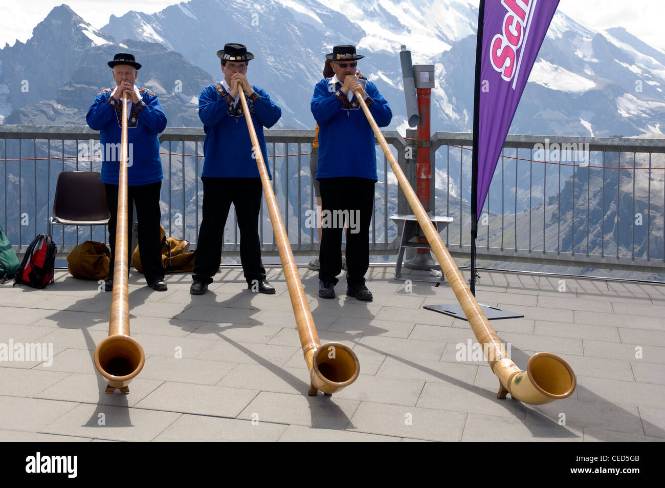 Chiudere orizzontale su ritratto di tre tradizionalmente condita gli uomini svizzeri la riproduzione del corno alpino con le Alpi svizzere dietro di loro. Foto Stock