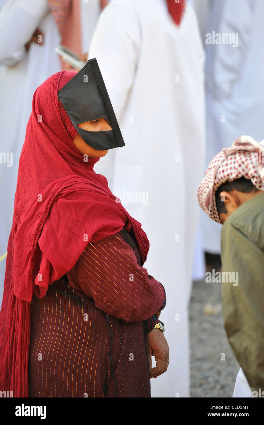 Una donna proveniente dalle colline con il suo viso e maschera in atmosferica di mercato del venerdì (capra) Mercato di Nizwa; Al Dakhiliyah, Oman. Foto Stock