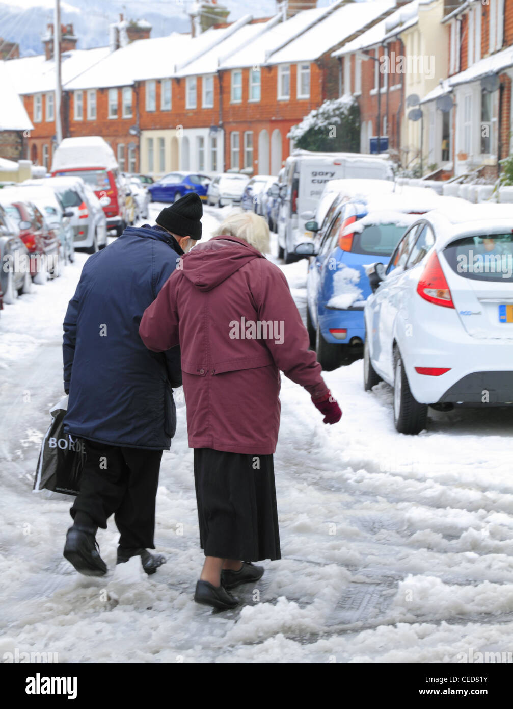 Il vecchio gli anziani giovane uomo e donna e i pensionati a piedi attraversando la strada in snow ice UK pericoloso inverno sdrucciolevole Foto Stock