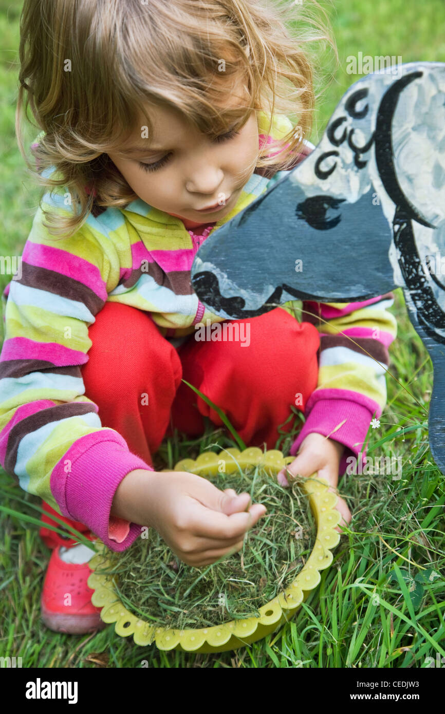 Graziosa Bambina alimenta il cavallo di legno in giardino Foto Stock