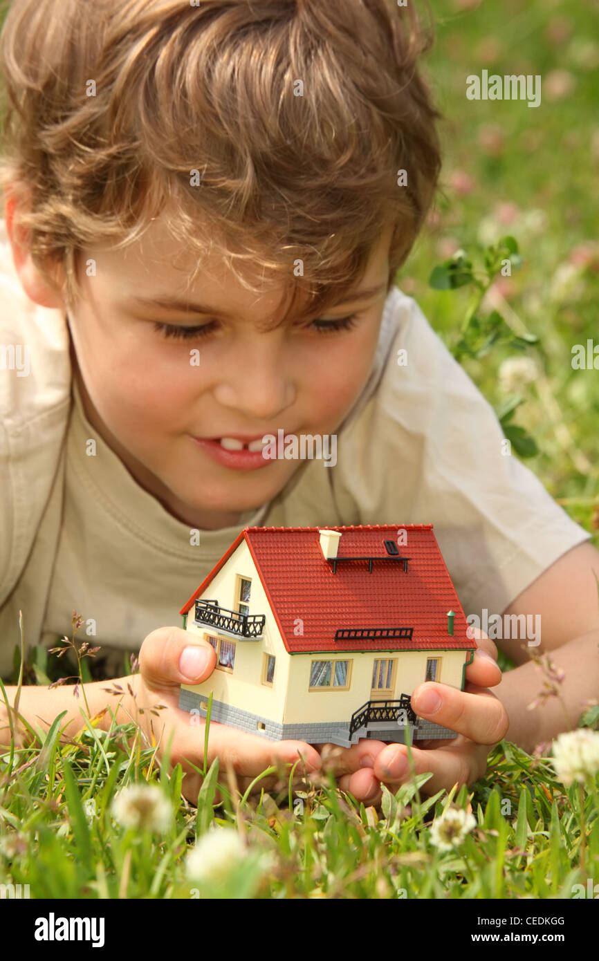 Ragazzo risiede in erba con modello di casa in mani Foto Stock