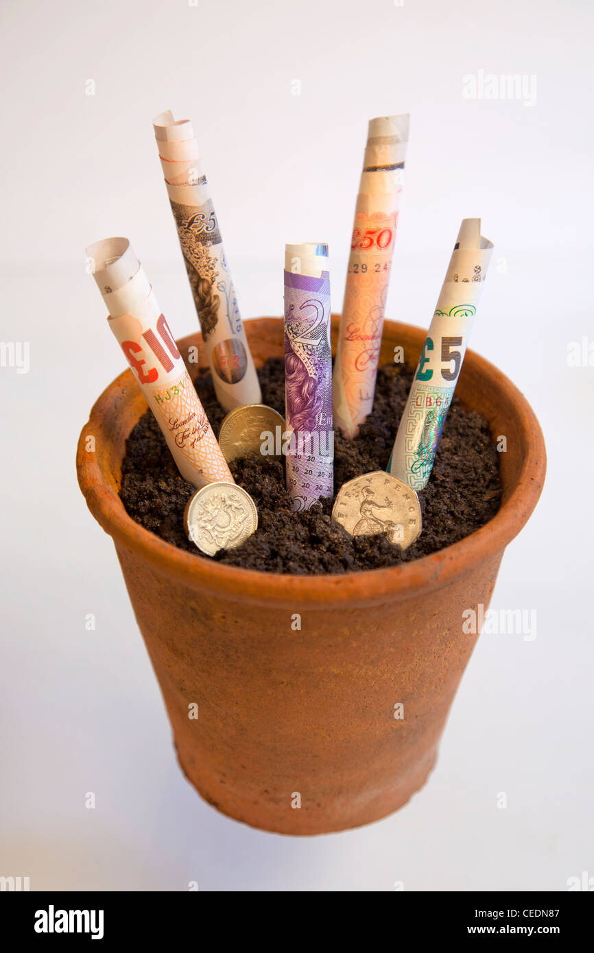 Rotoli di inglese sterline e monete valuta il denaro cresce in una pentola di terracotta Foto Stock