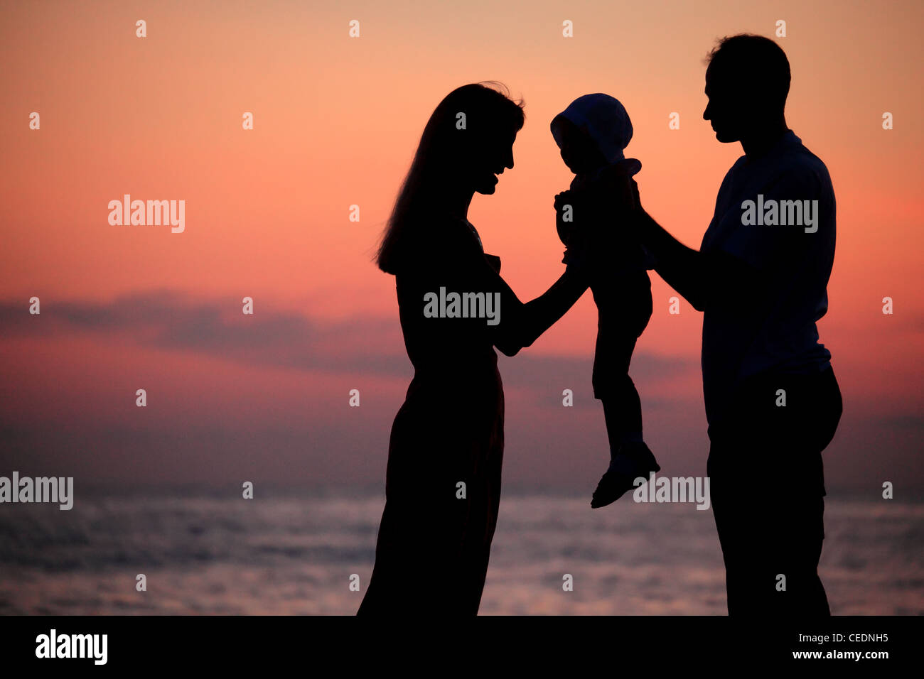 Sagome dei genitori con il bambino sulle mani contro il declino del mare Foto Stock