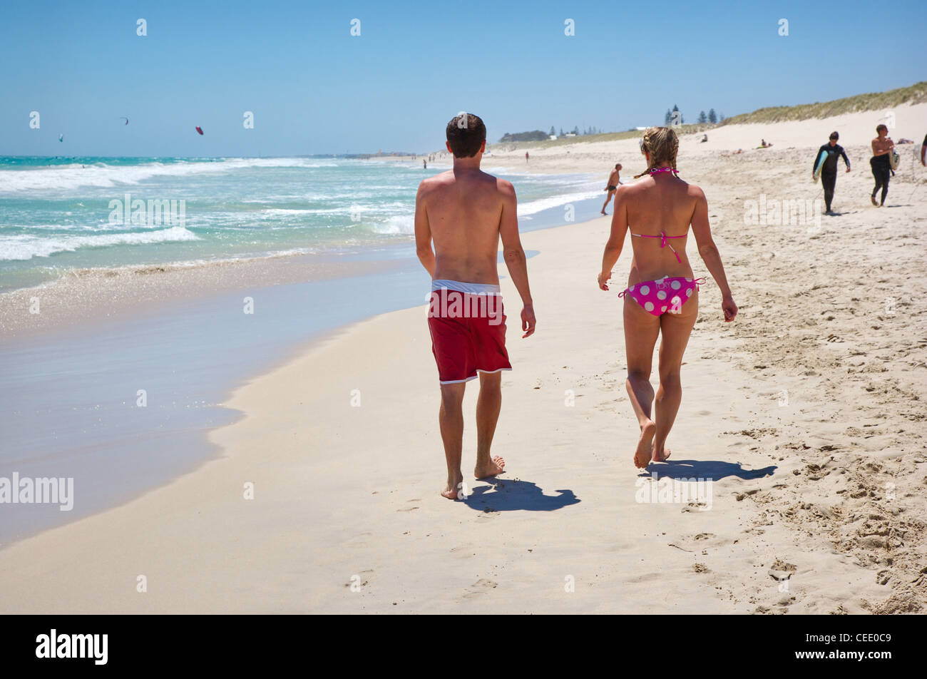 Un giovane uomo e donna che cammina lungo il sole inzuppato Scarborough Beach vicino a Perth Australia Occidentale Foto Stock