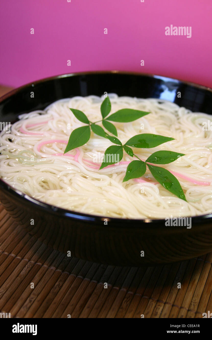 Cotte, preparate autentica cucina Giapponese, cibo, piatti. Colore rosa somen noodles nella ciotola nero sulla parte superiore del luogo di bambù mat. Foto Stock