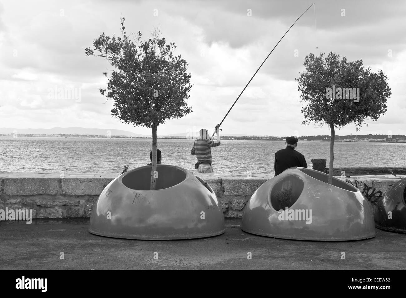 Tre uomini siedono dall'acqua del fiume Tejo a Lisbona, se quella che è la pesca. Cais do Sodre, Lisbona, Portogallo Foto Stock