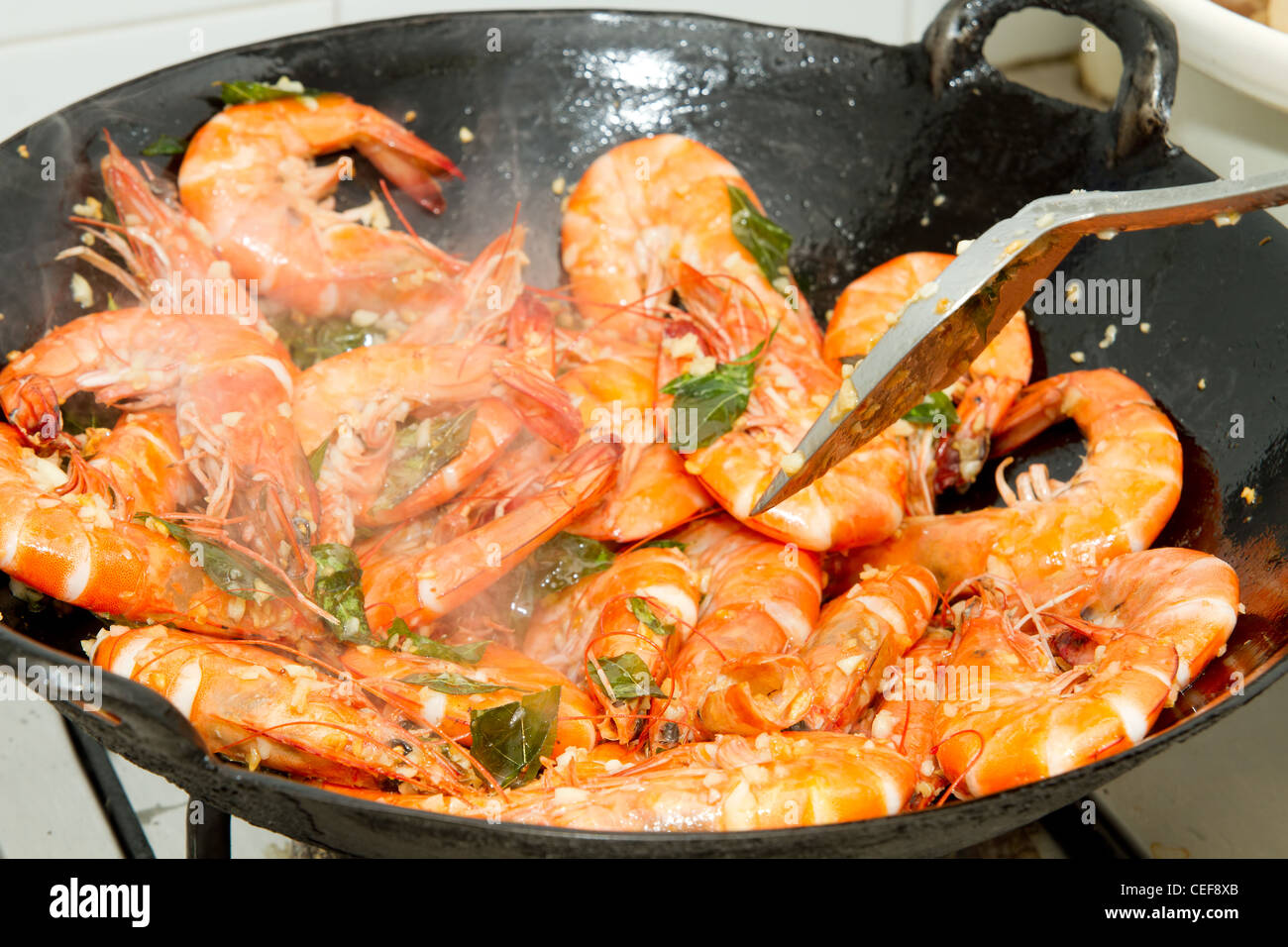 Friggere i gamberi con foglie di curry e aglio in un wok Foto Stock