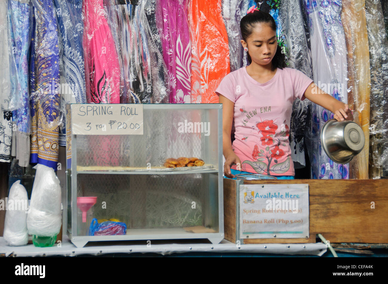 Asian filippino girl teen vendere involtini primavera nella parte anteriore di merci secche negozio tessile - Sabang Puerto Galera Filippine Foto Stock