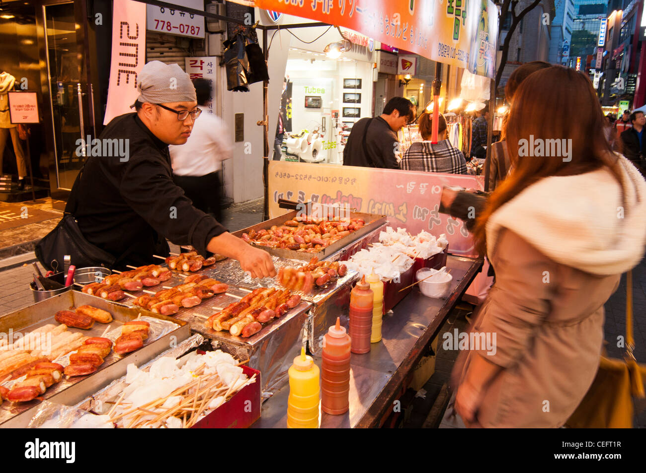 Strade cibo bancarelle che vendono vari cibi e spuntini in serata nel famoso quartiere dello shopping di a Myeongdong a Seul Foto Stock