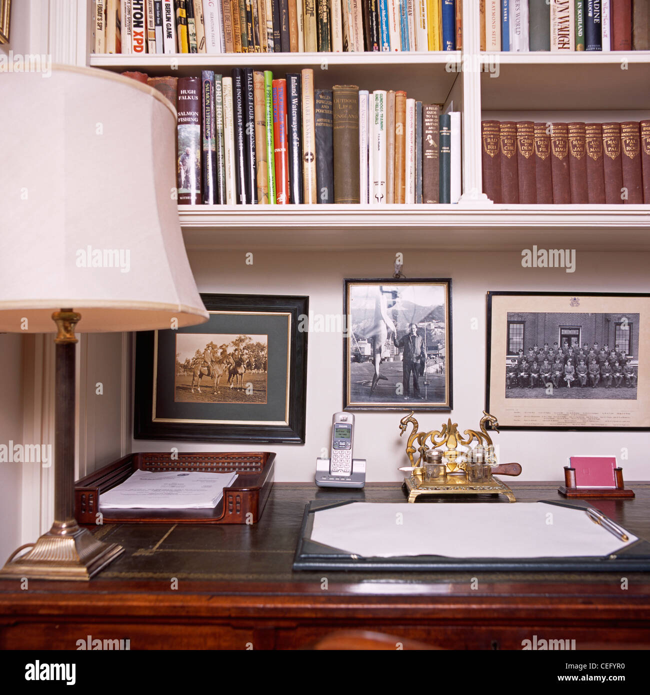 Lampada su antica scrivania sotto fotografie incorniciate e scaffali in studio tradizionale Foto Stock