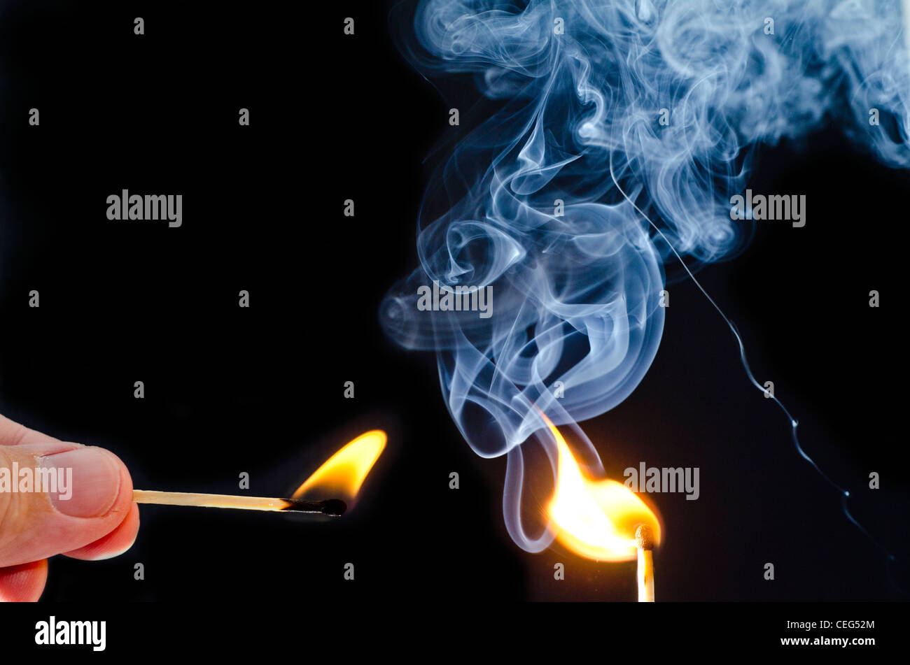 Illuminazione uomo una corrispondenza con un altro match, con fumo blu rising contro uno sfondo nero. Foto Stock