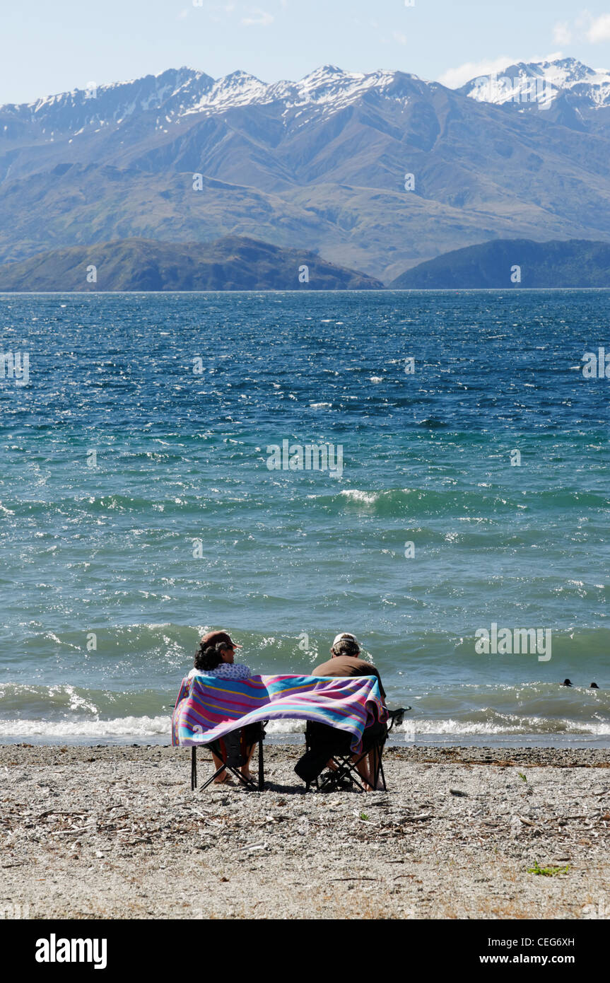 Un giovane seduto sul lago Wanaka Beach, Wanaka Nuova Zelanda Foto Stock