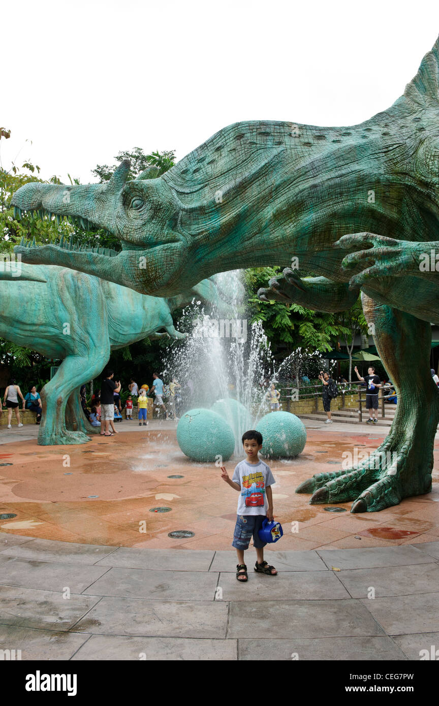 Bambino in posa dalla statua di dinosauro, Universal Studios Singapore. Foto Stock