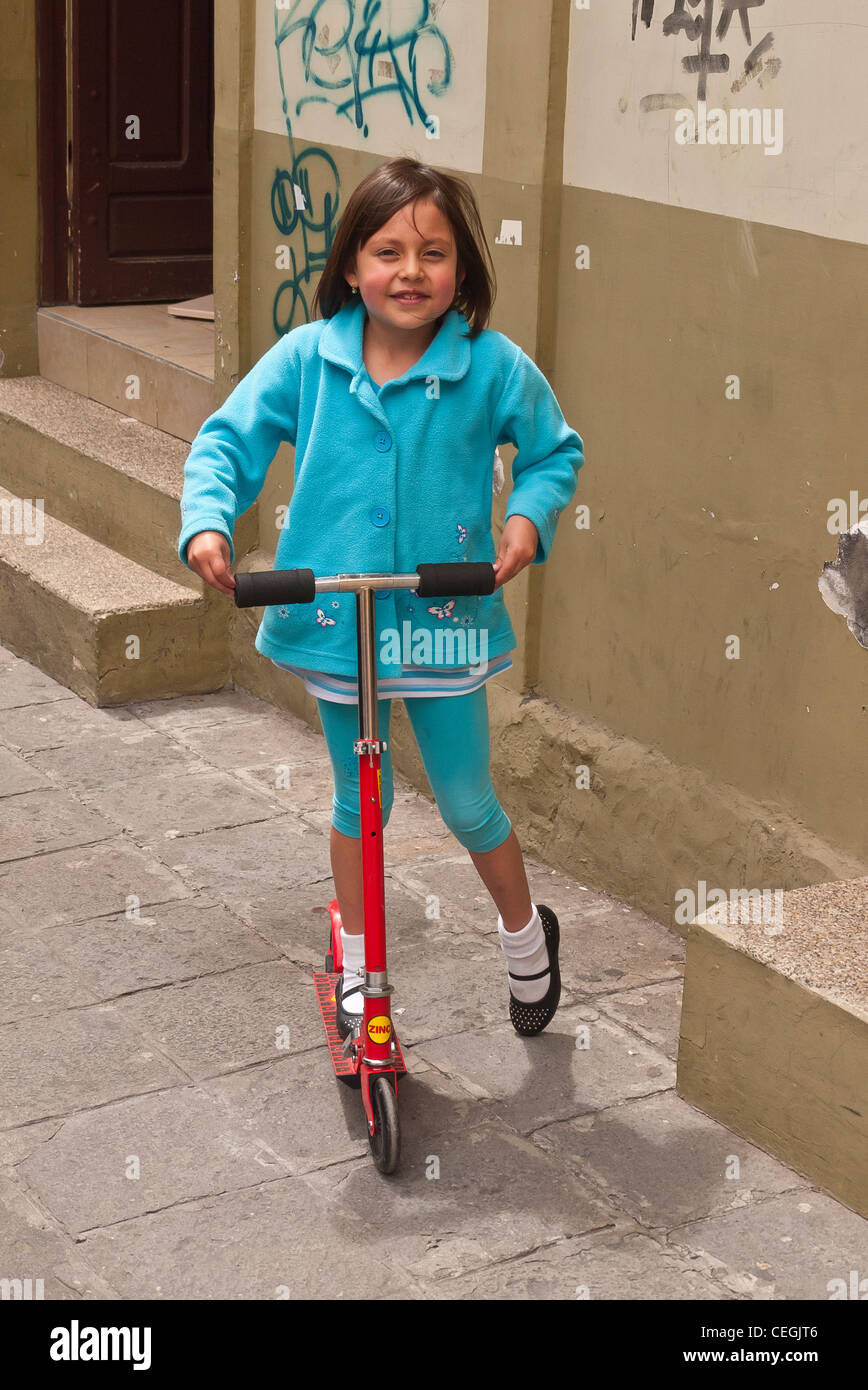 Un 10-12 anni ragazza ecuadoriana cavalca il suo scooter di rasoio al di fuori di casa sua in Latacunga, Ecuador. Foto Stock