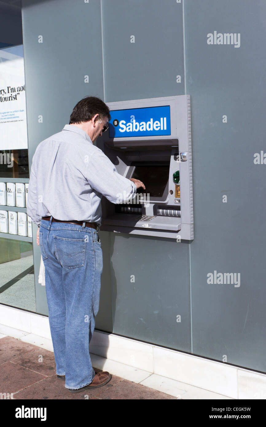 L'uomo il ritiro di denaro presso il Banco Sabdell bancomat in Spagna. Foto Stock