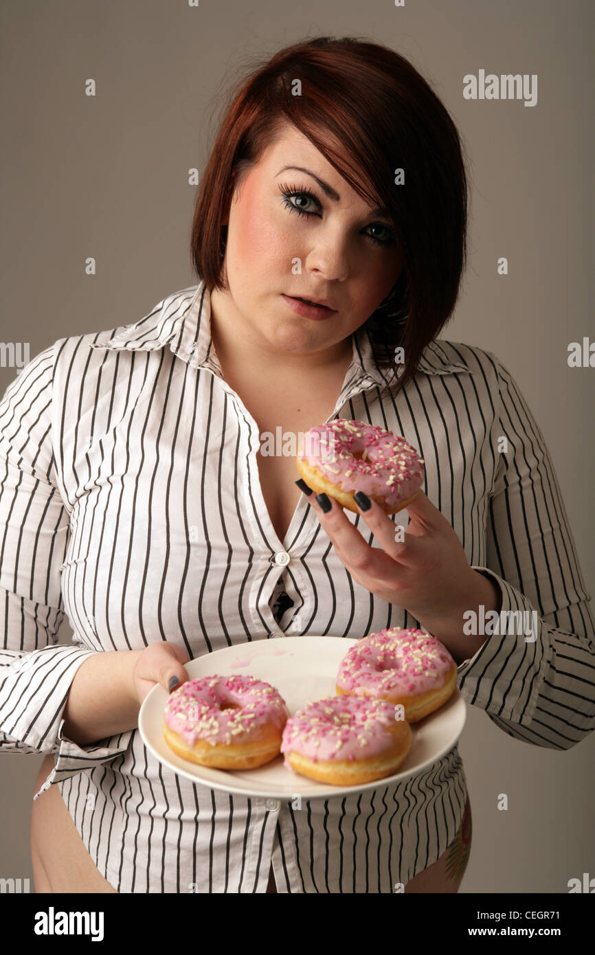 Donna sovrappeso tenendo un piatto di ciambelle. Foto Stock