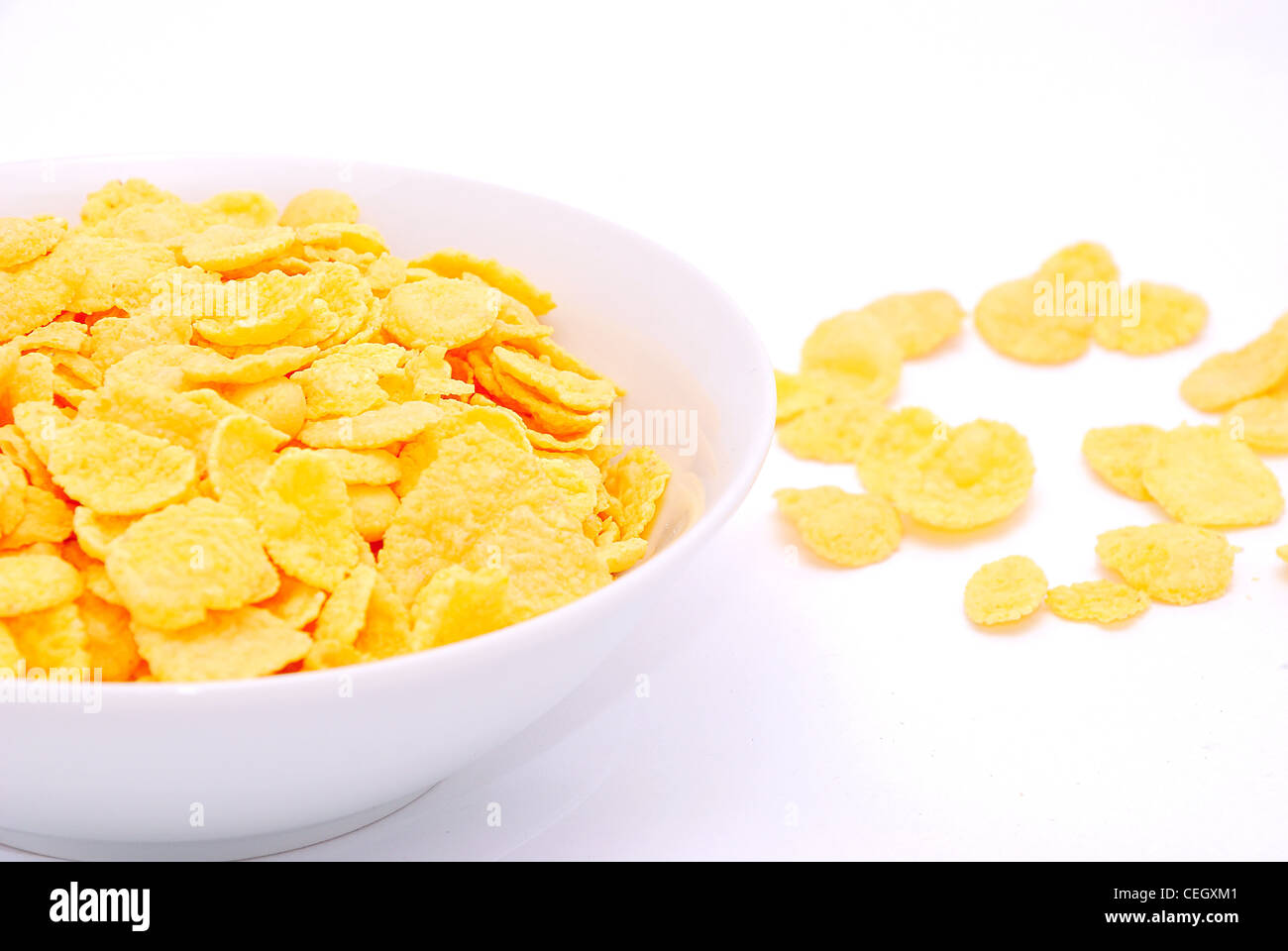 Oro fiocchi di mais ammucchiati in bianco e piatto sul tavolo bianco. Foto Stock