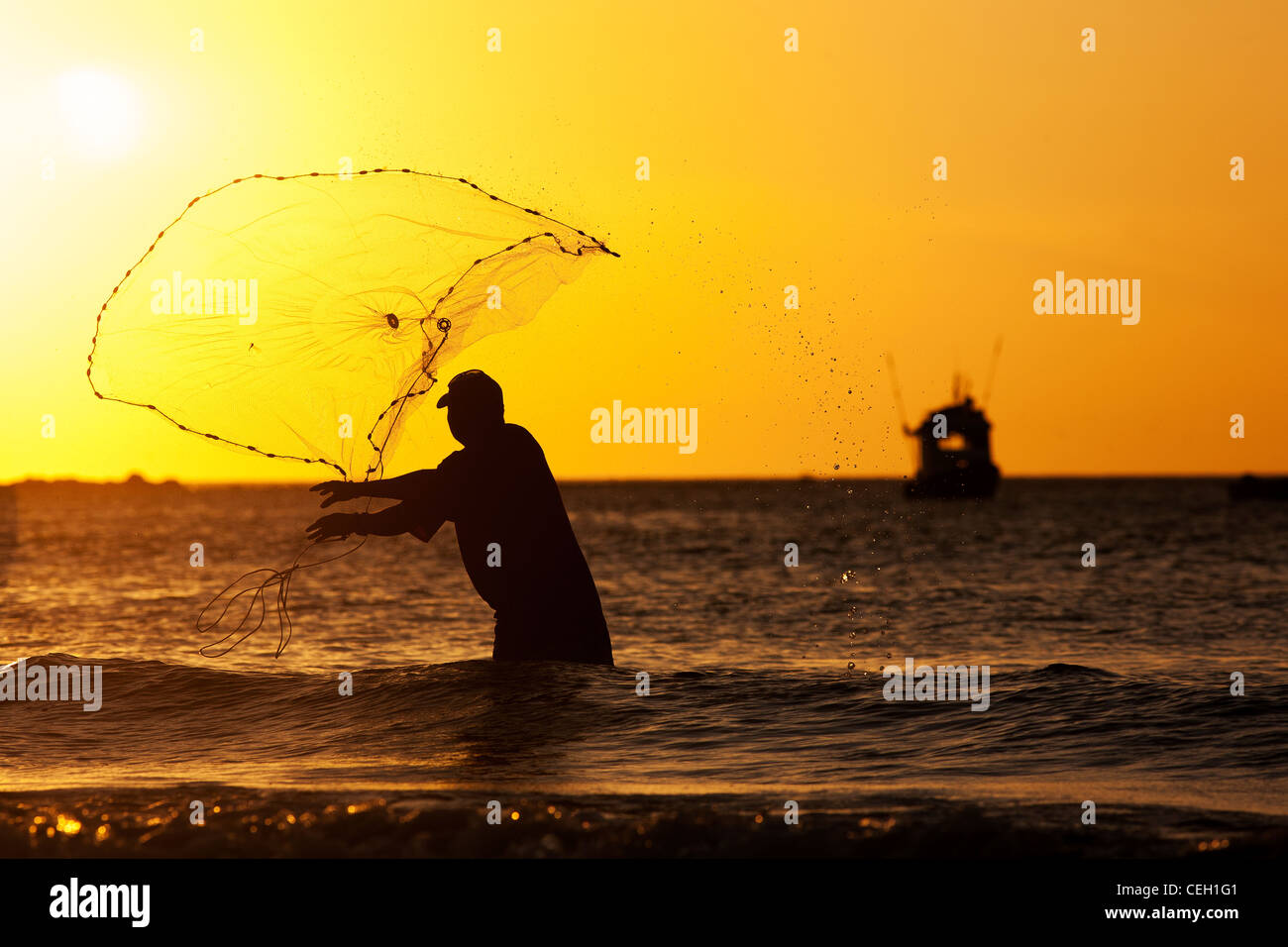Una Costa Rican uomo getta o getta una rete da pesca sulla spiaggia a Playa Tamarindo in Costa Rica al tramonto. Egli si stagliano Foto Stock