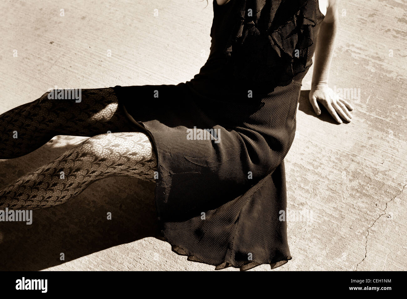 Bianco e nero donna seduta sulla pavimentazione indossando un vestito e collant, mano gamba piega del vestito Foto Stock