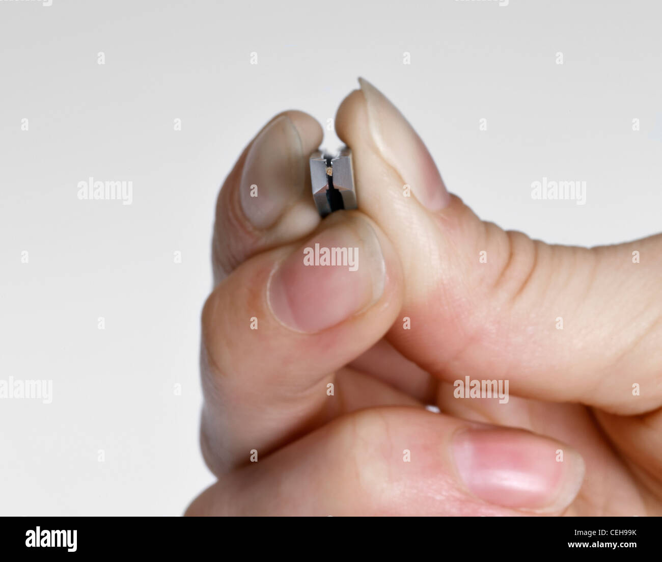 Mano femminile tenendo un paio di pinzette di presa di una piccola scheggia in grigio chiaro indietro Foto Stock