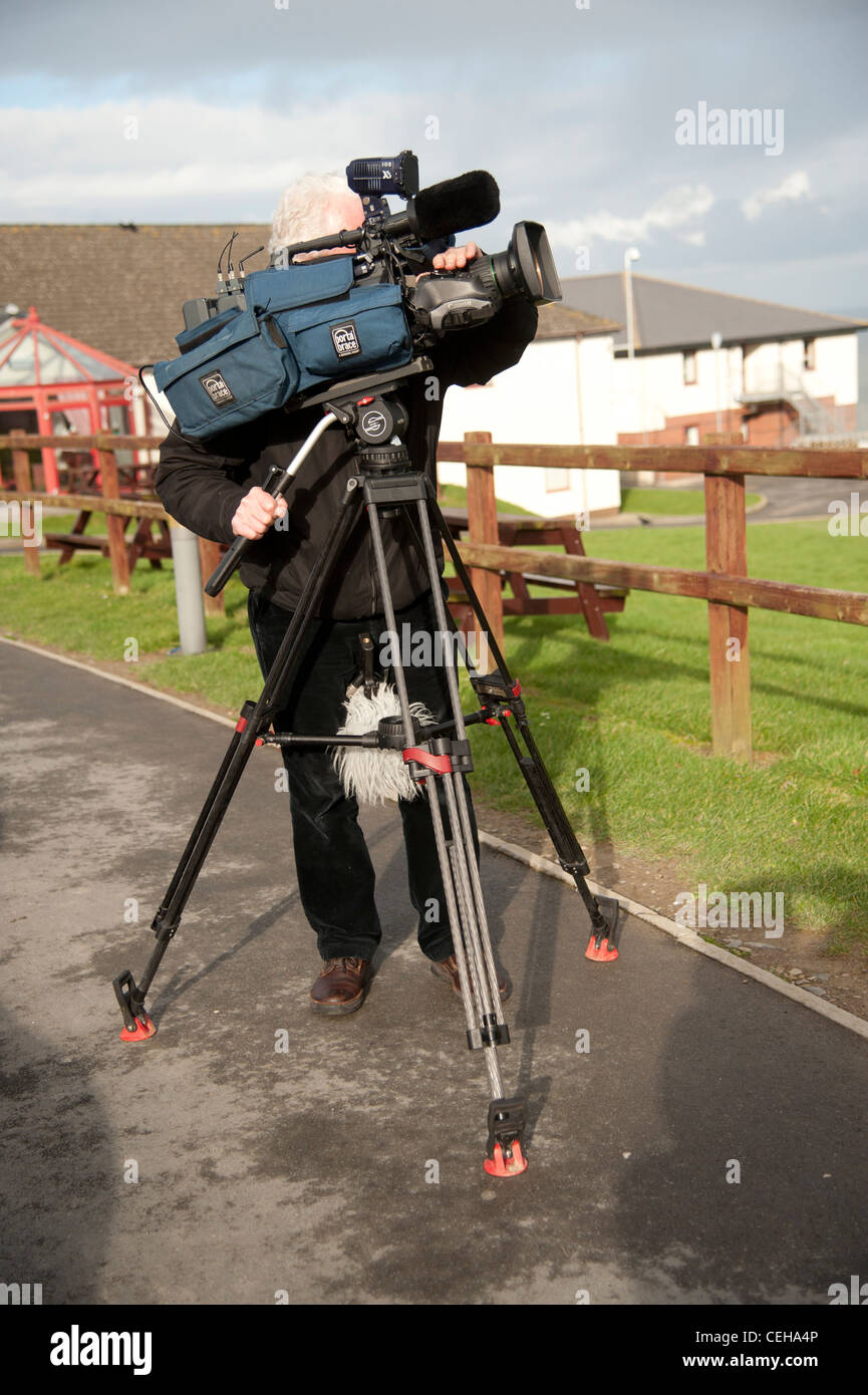 Una televisione video news cameraman con la sua telecamera su un treppiede, esterni al di fuori del Regno Unito Foto Stock