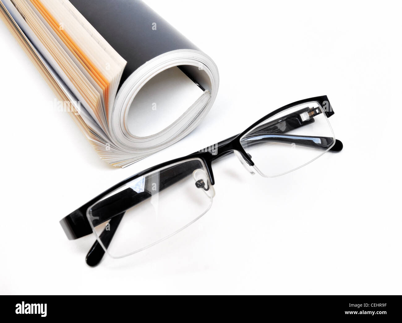 Arrotolato magazine con gli occhiali su sfondo bianco Foto Stock