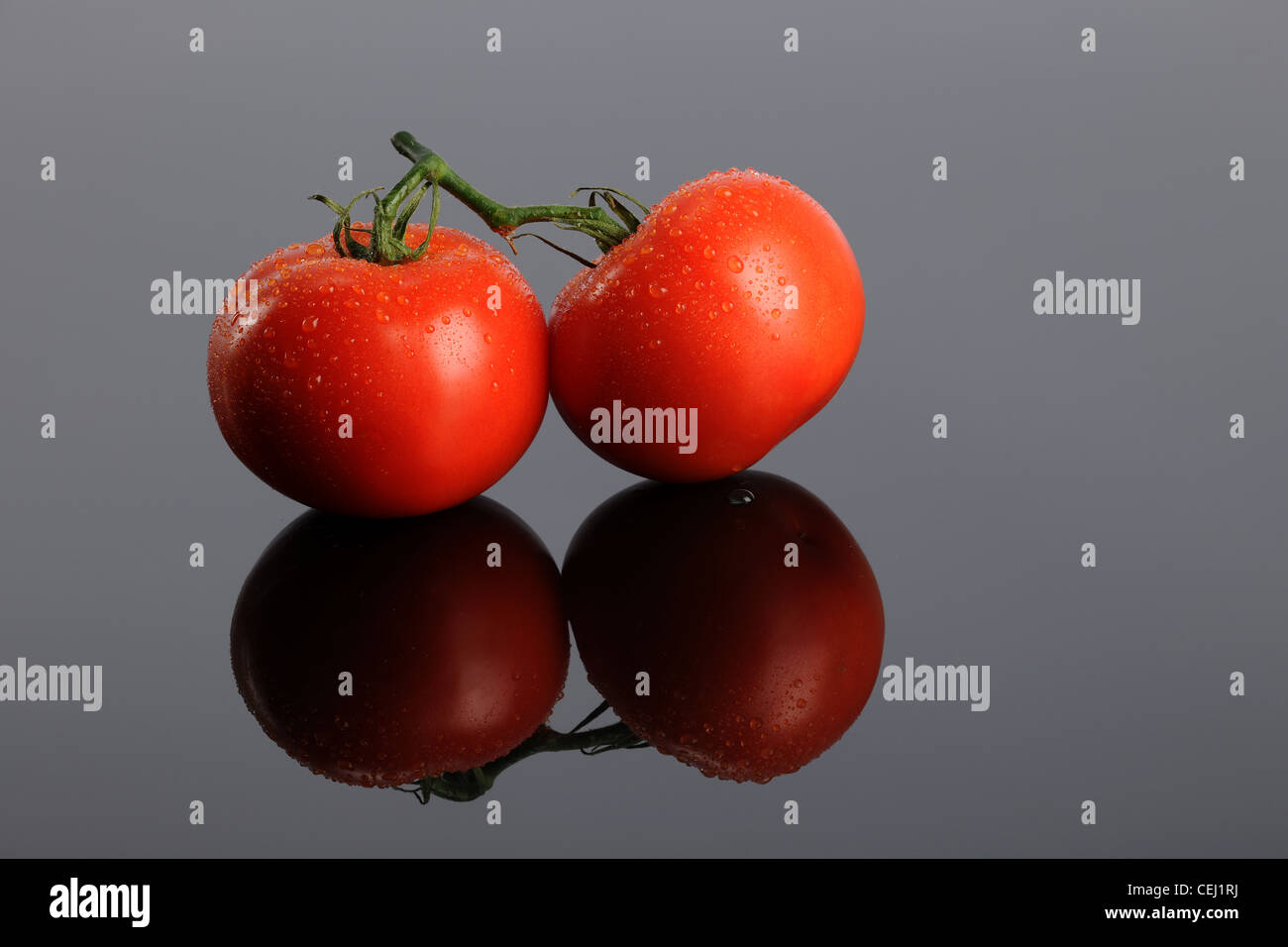 Due pomodori rossi su un Riflettente superficie grigia Foto Stock