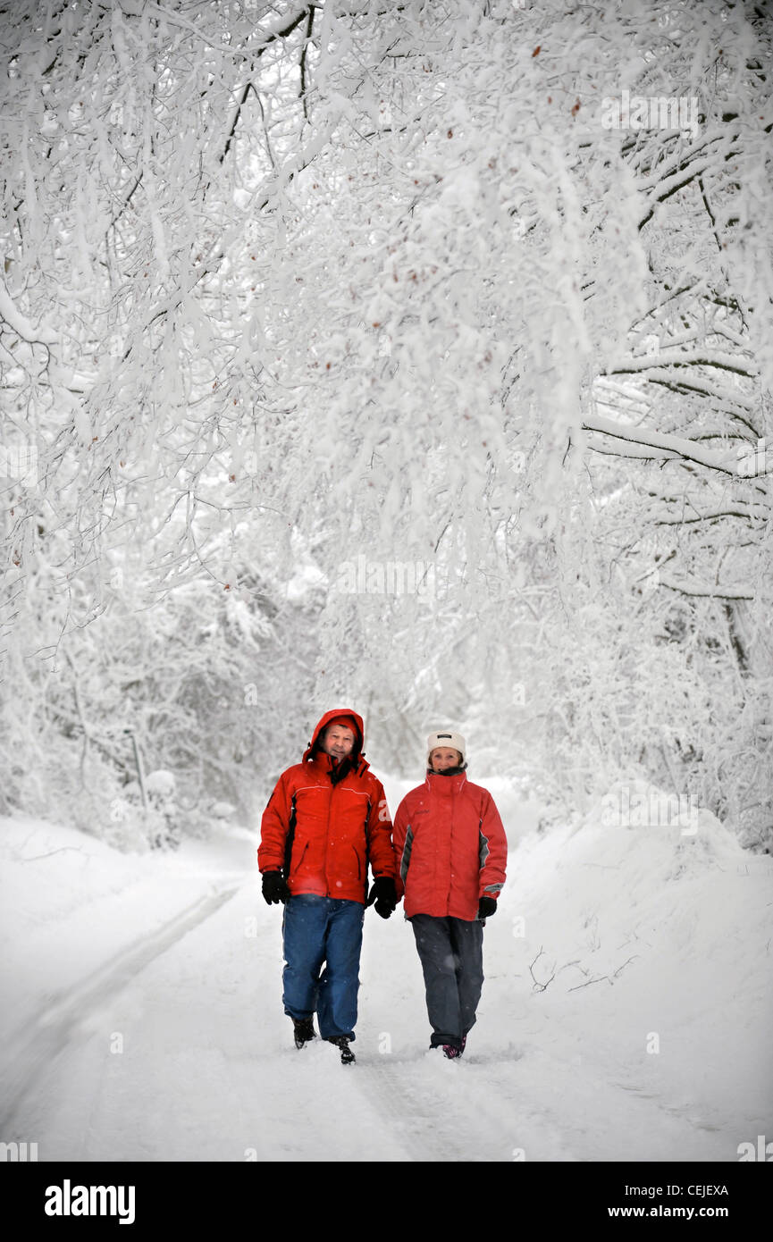 Un paio di matching red cappotti invernali a camminare in una corsia di Cotswold in condizioni nevoso REGNO UNITO Foto Stock
