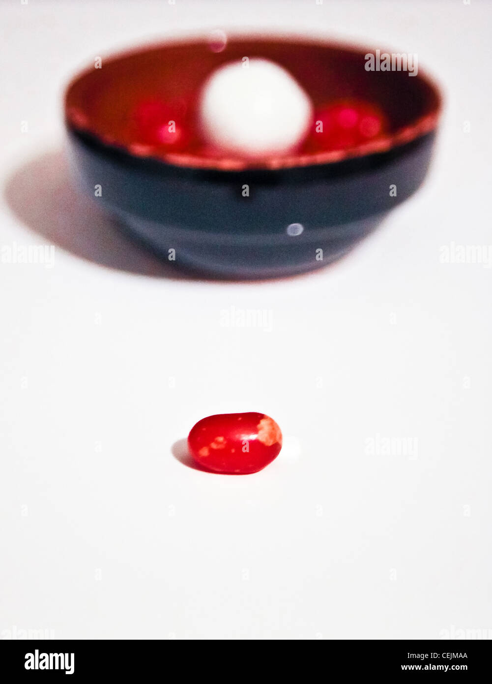 Rosso caramella da soli di fronte a un vaso di terracotta piena di colorati e alla cannella caramelle contro white Foto Stock