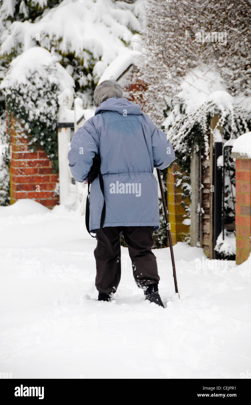 Titolare di pensione o di rendita con bastone da passeggio sul marciapiede nella neve profonda Foto Stock