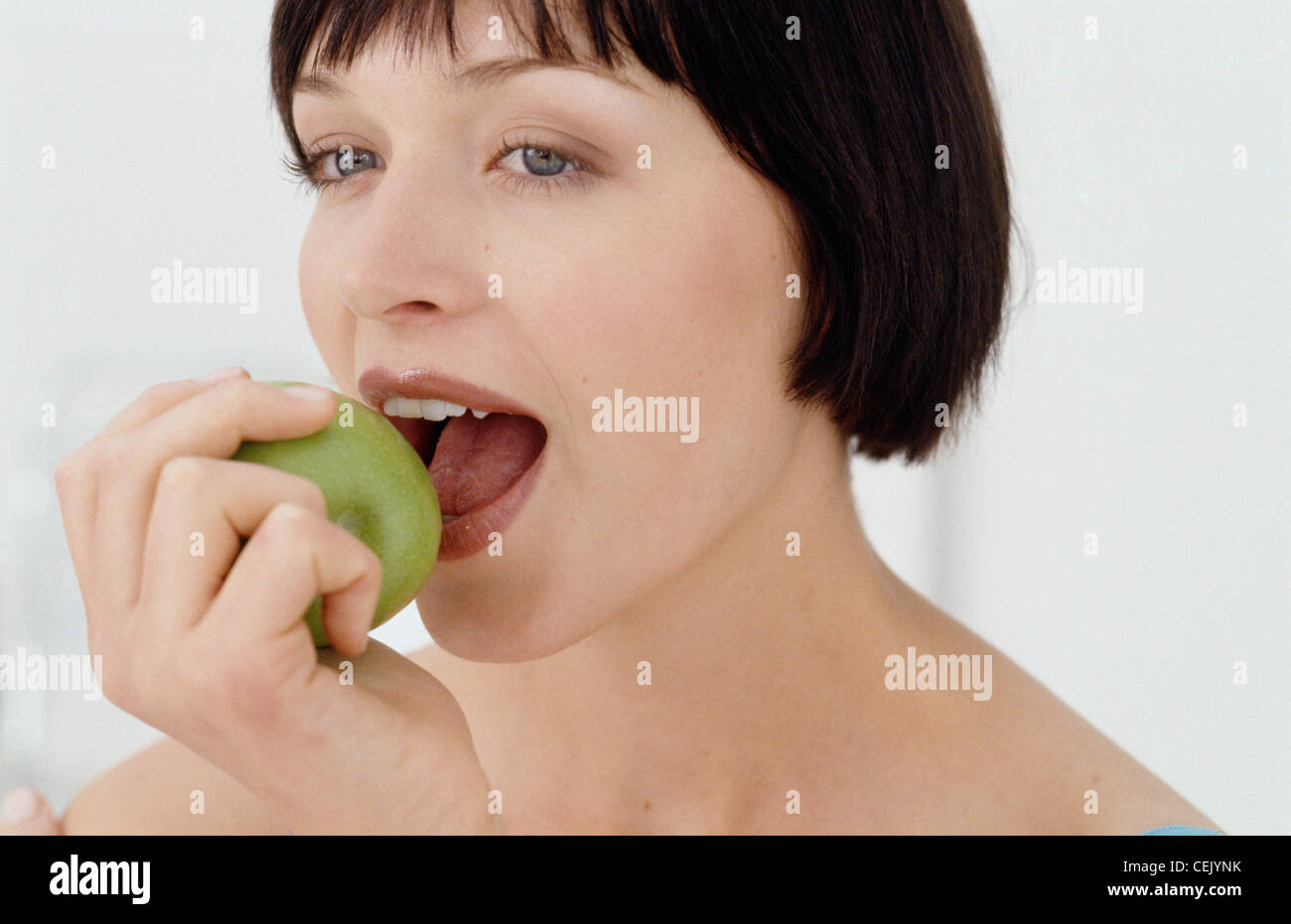 Una donna che guarda a sinistra di mordere una mela verde Foto Stock
