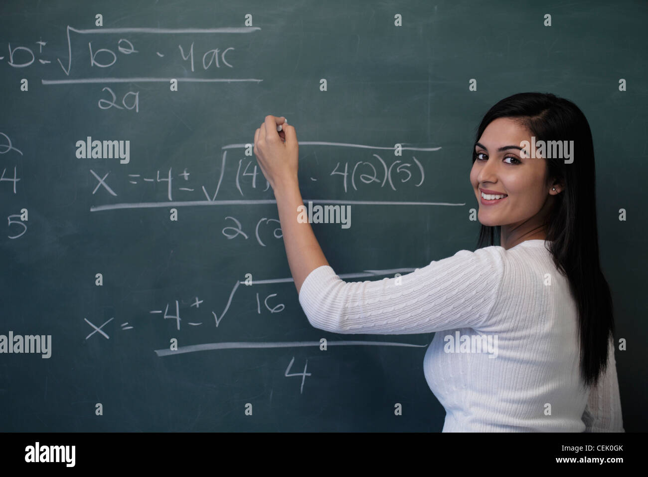 Giovane donna di scrittura equazione matematica su chalk board e sorridente Foto Stock