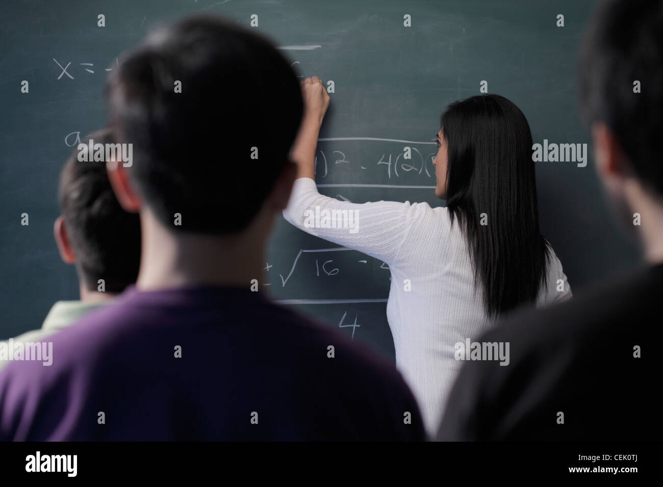 Vista posteriore di studenti guardando insegnante di scrivere sulla scheda di Chalk Foto Stock
