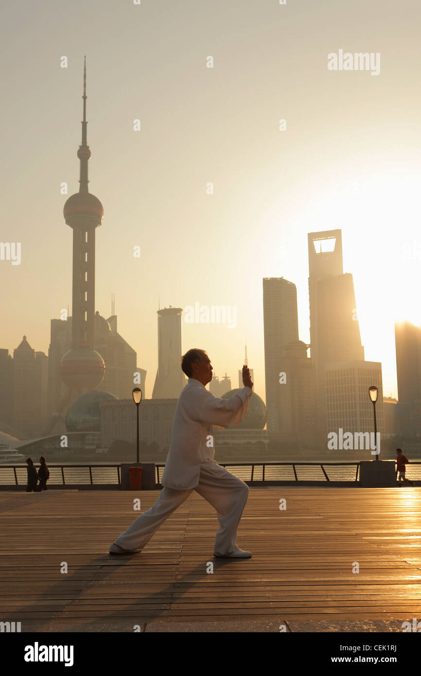 Uomo maturo facendo tai chi sul Bund a sunrise con lo skyline di Shanghai in background Foto Stock